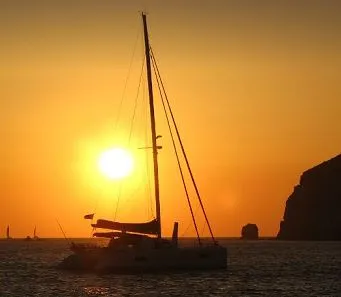 Segeln im Katamaran bei Sonnenuntergang Ein Katamaran segelt bei Sonnenuntergang über das Meer – mit der untergehenden Sonne im Hintergrund.