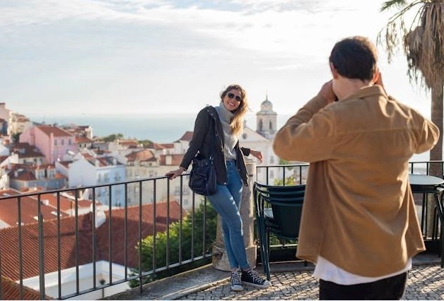 Touristen, die Fotos auf einem Aussichtspunkt mit einem Dorf im Hintergrund machen.