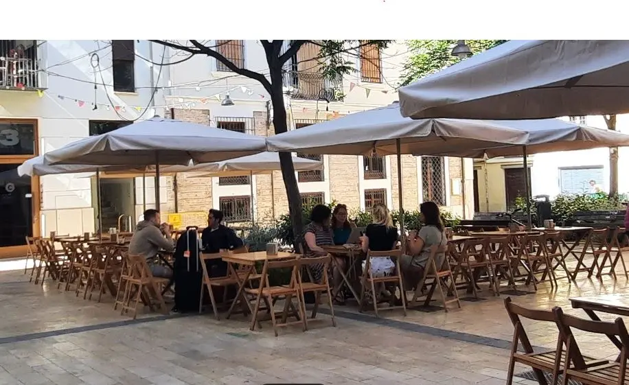Touristen sitzen auf der Terrasse einer Bar an einem Platz in Valencia.