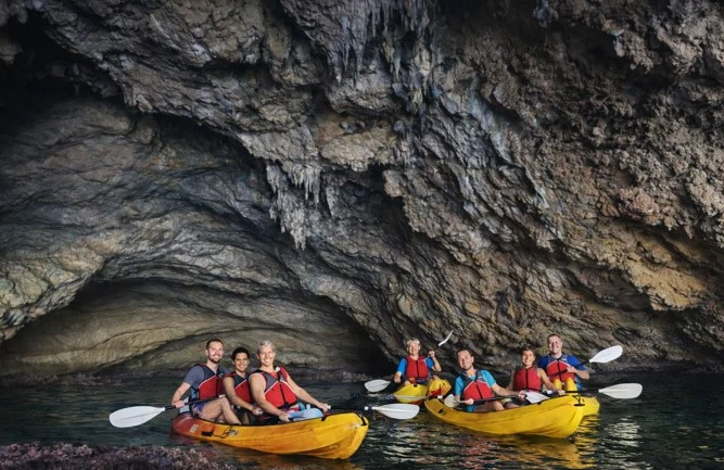 Gruppe von Touristen paddelt mit Kajaks in einer beeindruckenden Meereshöhle bei der Cala Granadella in Jávea, umgeben von Felsformationen und ruhigem Wasser.