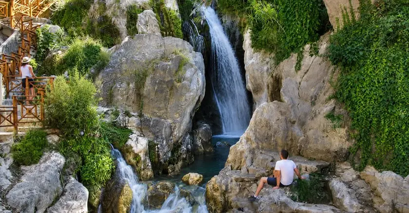 Tourist an den Fuentes del Algar zwischen Wasserfällen, türkisfarbenen Naturbecken und mediterraner Vegetation in der Nähe von Guadalest.
