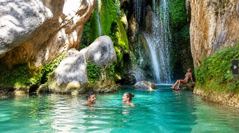 Touristen schwimmen in türkisfarbenem Wasser an den Wasserfällen von Algar in Alicante, umgeben von Felsen, grüner Vegetation und natürlicher Landschaft.